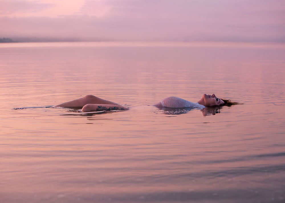 Woman floating in water at sunrise.  Shades of pink & purple 