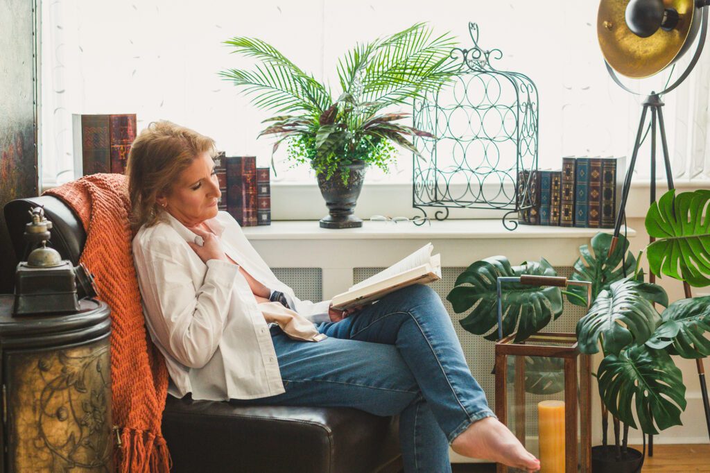 portrait of a woman sitting in a chair reading a book in everyday clothing with her ileostomy bag showing