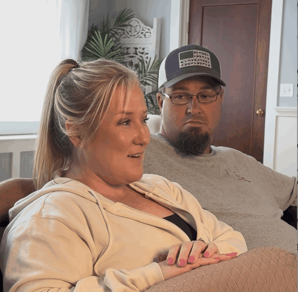 A couple sitting on a couch, where the woman is smiling, looking at her photos, while her husband looks on in support at a Massachusetts body image photographer studio
