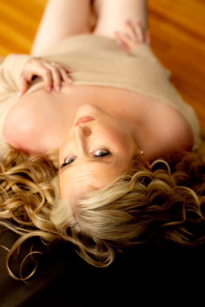 Blonde-haired woman lying on the floor looking up at a Massachusetts body image photographer 